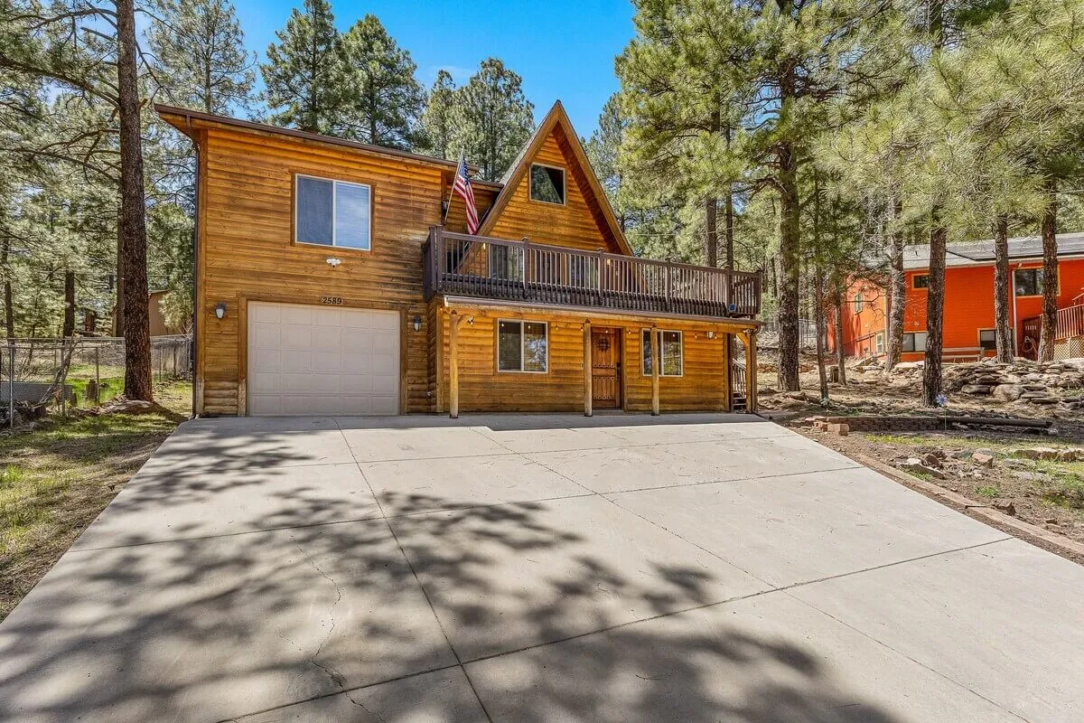 This image highlights the cabin’s A-frame design, a prominent balcony overlooking surrounding nature, large windows, and a driveway suggesting easy access for excursions. The scene exudes a welcoming, adventure-ready vibe, and the balcony offers a lookout to the nearby forests and red rocks mentioned in the section.