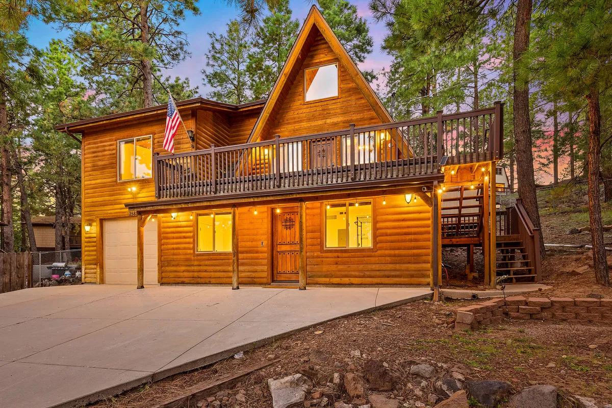 This exterior view showcases the cabin’s A-frame architecture, large windows reflecting the sky, a spacious wooden deck, and the American flag. The scene hints at family gatherings, sunset views, and easy access to the outdoors, with visual cues that evoke relaxation after a day of exploring nearby attractions.